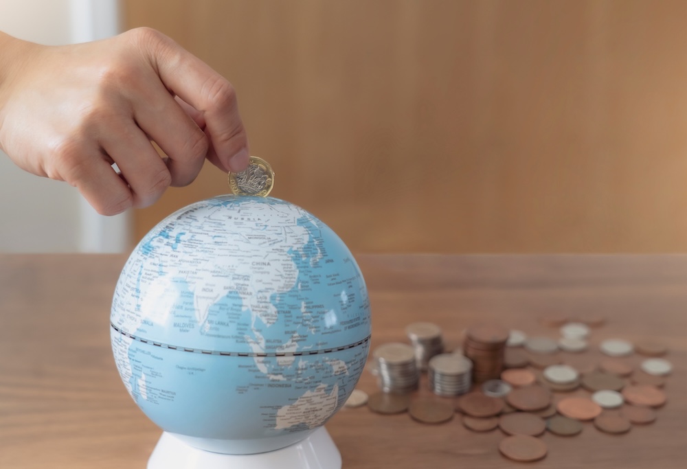 Hand putting money into a bank shaped like the earth