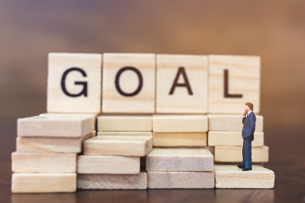 Miniature business person looking at letters spelling GOAL