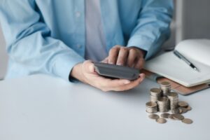 Person with a calculator and a stack of coins on a desk