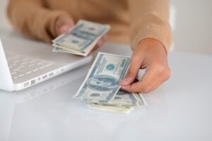 Young person counting cash near laptop