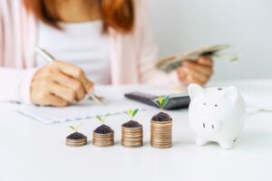 Young woman calculating her expenses with stacked coins and a piggy bank