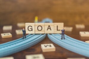 Miniature business people standing on a wooden roads with the word goal