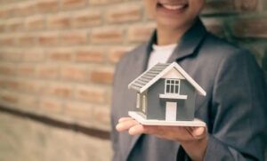 Woman smiling and holding a small house in her hand