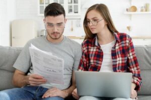 Couple looking at paperwork sitting on the couch using a laptop