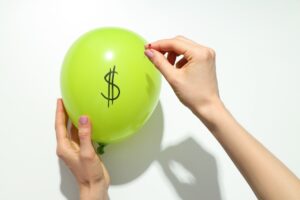 hands popping a balloon with a dollar sign on it