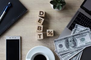 debt % spelled in wooden blocks with cash and smartphone on table