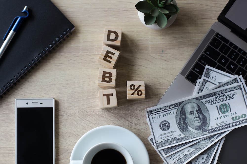 debt % spelled in wooden blocks with cash and smartphone on table